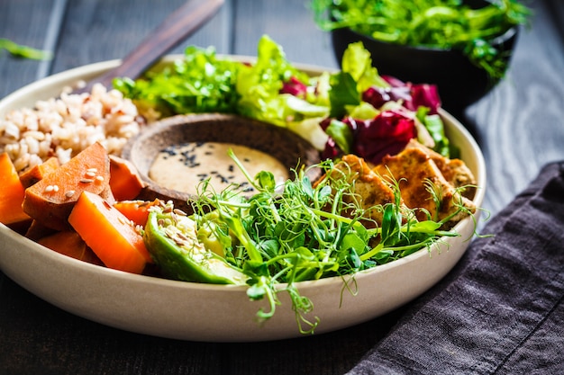 Bol de Bouddha avec tofu, avocat, riz, plants, vinaigrette à la patate douce et au tahini.