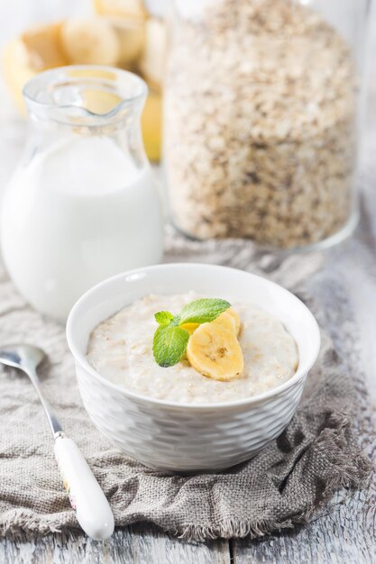 Bol de bouillie d'avoine avec banane sur table rustique en bois blanc, petit-déjeuner sain, alimentation diététique.