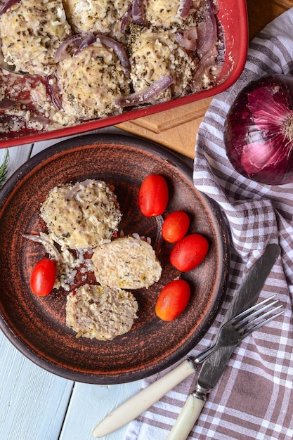 Un bol de boulettes de viande avec des tomates et des oignons à côté d'un oignon rouge.