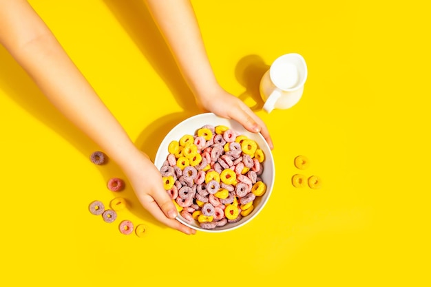 Photo un bol de céréales de maïs colorés sur une table jaune concept de petit déjeuner mains d'enfant tenant un bol