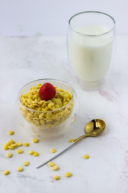 Un bol de céréales pour petit-déjeuner et un verre de lait sur une table en marbre blanc Flocons de maïs instantanés aux fraises