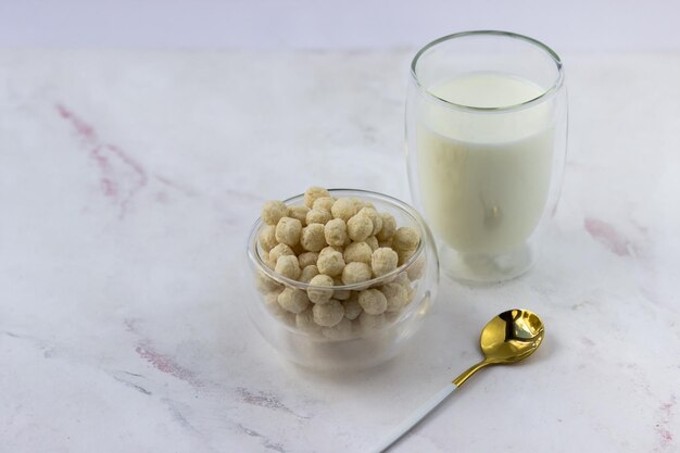 Un bol de céréales pour le petit déjeuner et un verre de lait sur une table en marbre blanc Flocons de maïs instantanés