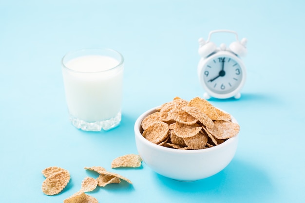 Un bol de céréales, un verre de lait et un réveil sur une table bleue. Petit déjeuner programmé