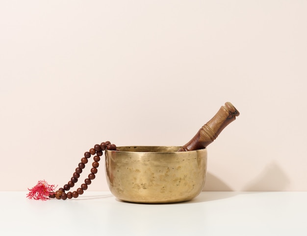 Bol chantant en cuivre et battant en bois sur une table blanche. Instrument de musique pour la méditation, la relaxation, diverses pratiques médicales liées aux biorythmes, normalisation de la santé mentale