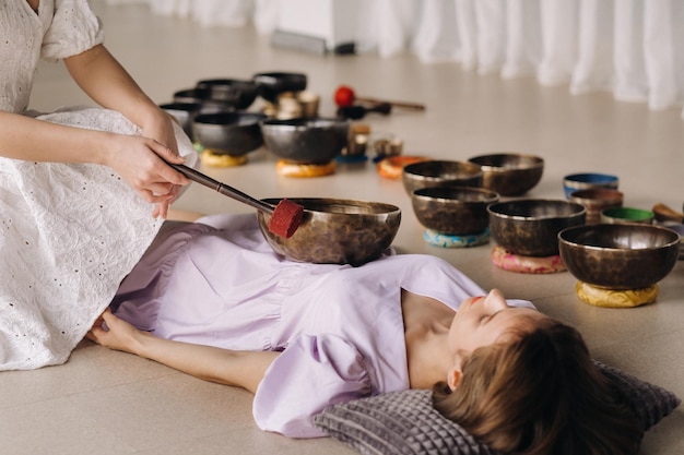 Le bol chantant en cuivre du Bouddha népalais dans le spa Une belle jeune femme fait un massage avec des bols chantants dans un salon de spa sur fond de cascade