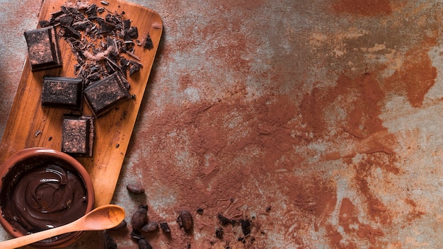 Photo bol de chocolat fondu et barre écrasée sur planche à découper avec une cuillère en bois