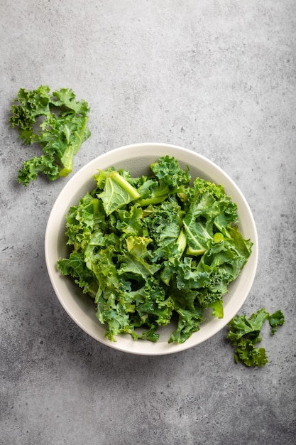 Bol de chou frisé vert frais sur fond de pierre rustique grise, vue de dessus, gros plan. Ingrédient pour faire une salade saine. Concept d'alimentation propre, de désintoxication ou de régime