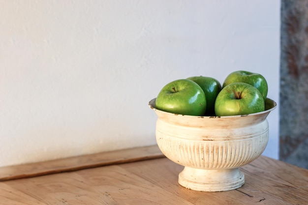 Photo bol con manzanas verdes sobre una barra de madera y una pared blanca a la luz del atardecer