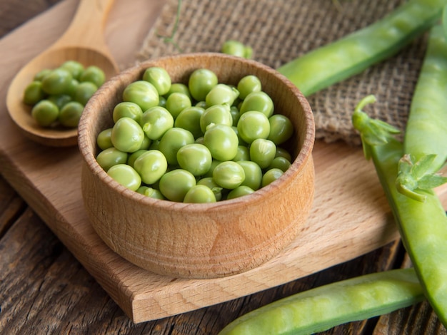 Bol et cuillère en bois avec des pois frais et leurs gousses sur une vieille table en bois fond rustique avec des pois