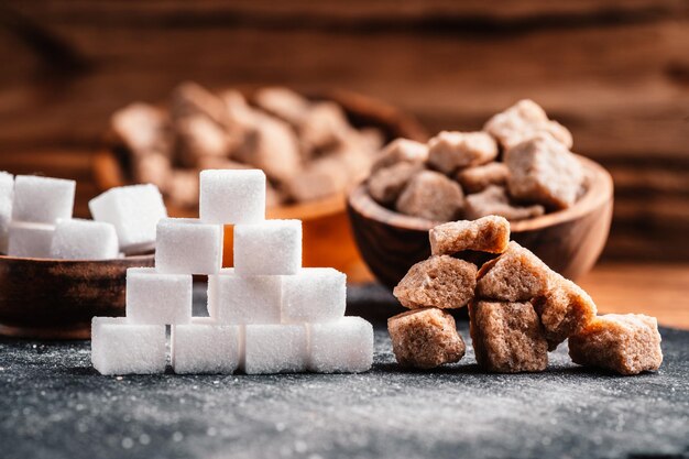 Bol et cuillère avec du sable blanc et du sucre blanc en morceaux sur fond de bois Cube de sucre brun Faire une alimentation malsaine, l'obésité, le diabète, les soins dentaires et bien plus encore