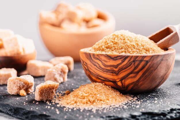 Bol et cuillère avec du sable et de la cassonade en morceaux sur fond de bois cube de sucre brun Faire une alimentation malsaine, l'obésité, le diabète, les soins dentaires et bien plus encore