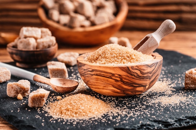 Bol et cuillère avec du sable et de la cassonade en morceaux sur fond de bois cube de sucre brun Faire une alimentation malsaine, l'obésité, le diabète, les soins dentaires et bien plus encore