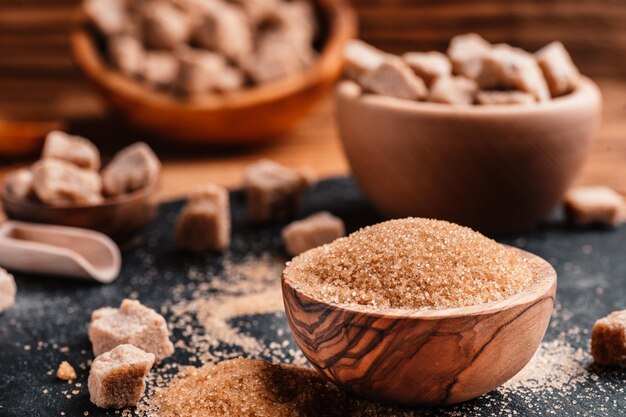 Bol et cuillère avec du sable et de la cassonade en morceaux sur fond de bois cube de sucre brun Faire une alimentation malsaine, l'obésité, le diabète, les soins dentaires et bien plus encore