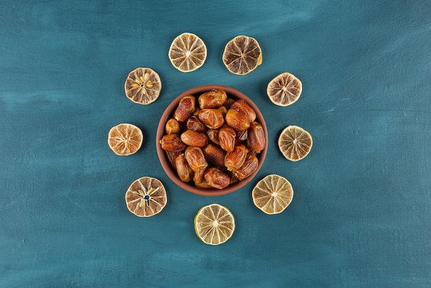 Bol de dattes séchées et tranches de citron sur table bleue.