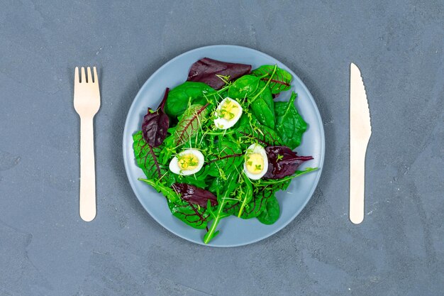 Photo bol à déjeuner de feuilles de laitue avec des œufs avec une fourchette et une cuillère en bois sur fond gris concept d'aliments sains pp vue de dessus zéro déchet