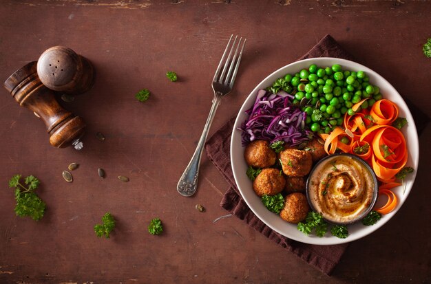 Bol déjeuner végétalien sain avec des rubans de carottes falafel houmous chou et petits pois