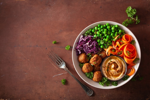 Bol déjeuner végétalien sain avec des rubans de carottes falafel houmous chou et petits pois