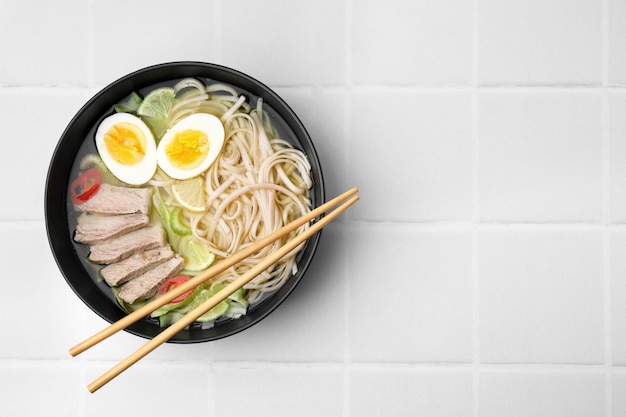 Bol de délicieuse soupe de nouilles de riz avec de la viande et des œufs sur la vue de dessus de table carrelée blanche Espace pour le texte