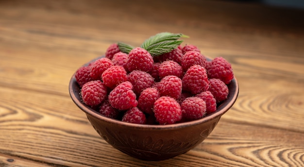 Bol avec de délicieuses framboises fraîches et mûres et une feuille verte sur un fond en bois