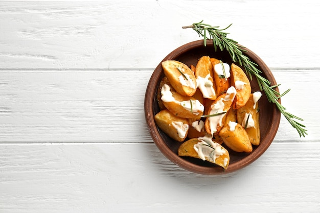 Un bol avec de délicieux morceaux de pommes de terre cuites au four sur fond de bois