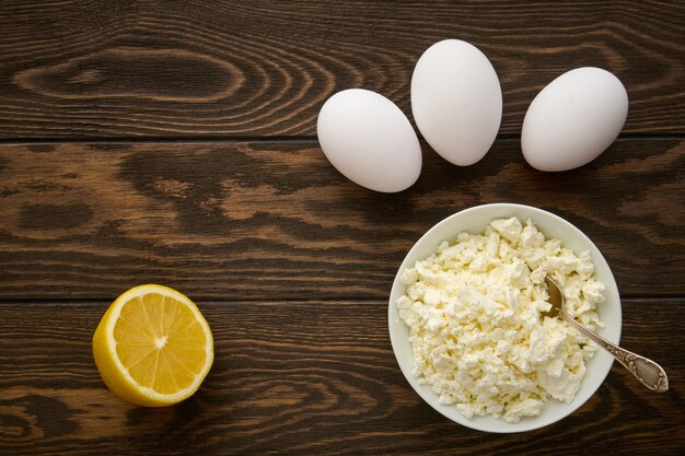 Photo bol avec du fromage cottage, des œufs de poule et du citron sur une table en bois