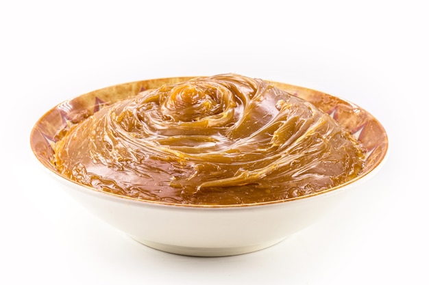 Bol avec dulce de leche fait maison, crème condensée ou caramel pâteux, fond blanc isolé.