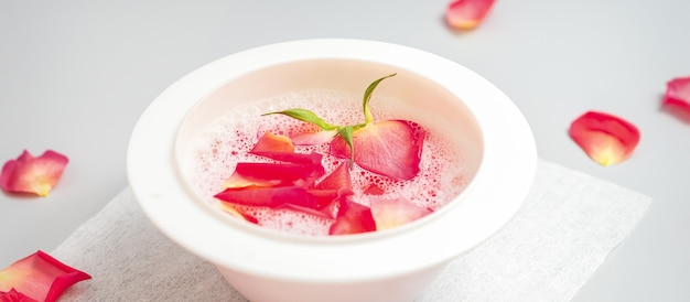 Un bol d'eau blanc avec des pétales de rose rose sur un tableau blanc dans le salon spa