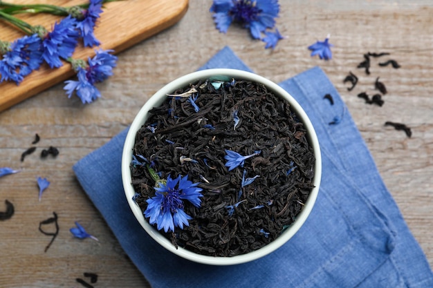 Bol avec des feuilles de thé sèches et des bleuets sur une table en bois à plat