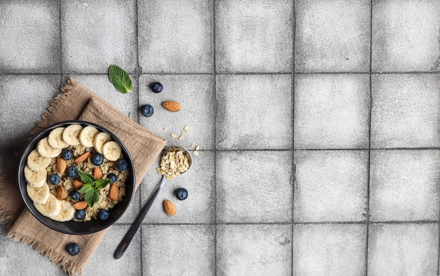 Un bol de flocons d'avoine avec des bleuets et des amandes sur un fond de carreaux gris.