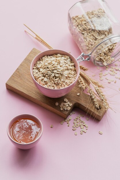 Bol de flocons d'avoine secs avec du miel et des épis de blé sur fond rose clair