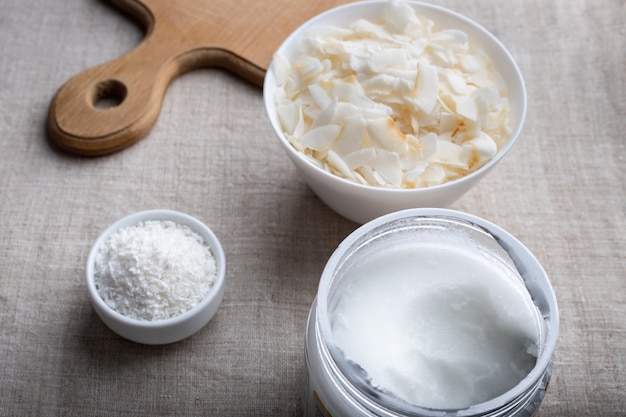 Bol de flocons de noix de coco et pot d'huile de coco sur tissu