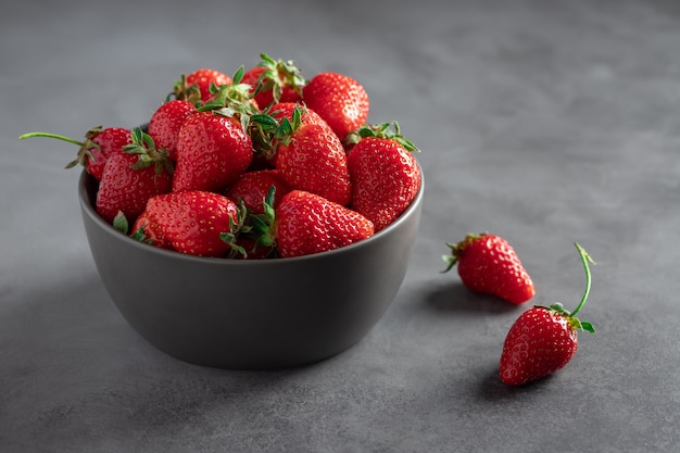 Bol foncé avec des fraises mûres. aliments vitaminés sains. mur de béton foncé. image horizontale