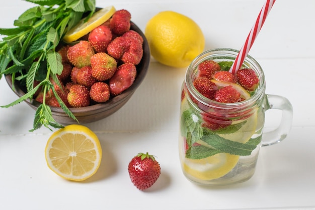 Un bol de fraises et une grande tasse d'eau froide et de citron sur un tableau blanc