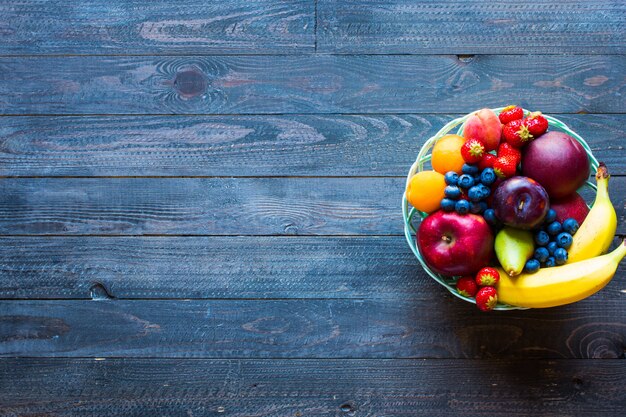 Bol de fruits frais avec banane, pomme, fraises, abricots, myrtilles, prunes, grains entiers, fourchettes, vue de dessus