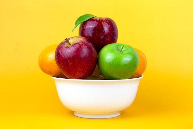 Un bol de fruits sains pommes vertes pommes rouges oranges isolées sur fond jaune et fruits exotiques délicieux dans un bol blanc sur fond jaune