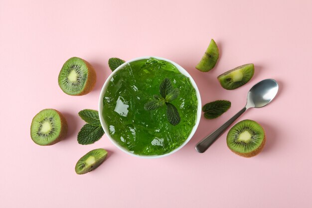 Bol de gelée de kiwi, tranches de kiwi, cuillère et menthe sur fond rose