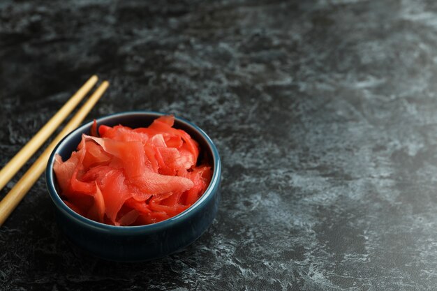 Bol avec gingembre mariné rouge et baguettes sur une surface fumée noire