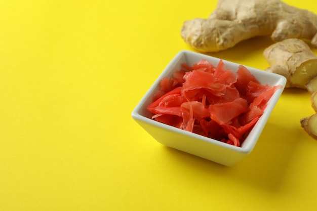 Bol avec gingembre mariné rouge et gingembre sur une surface jaune