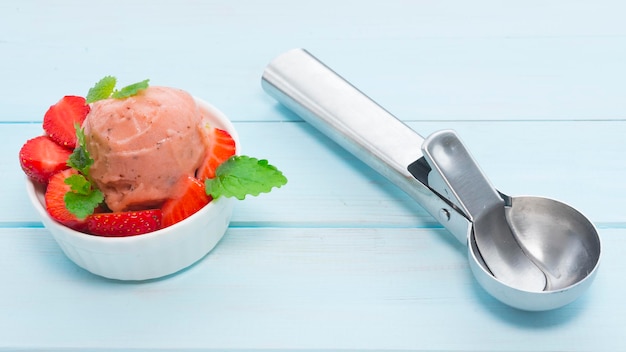 Un bol de glace à la fraise et une cuillère à glace se trouvent à proximité