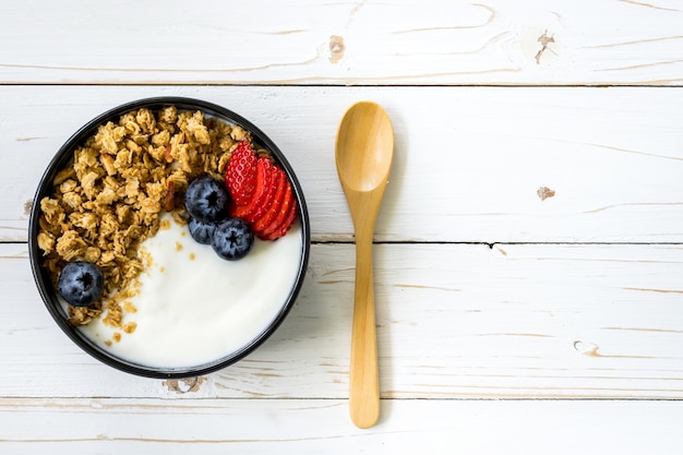 bol de granola au yogourt, baies fraîches, fraises sur table en bois.