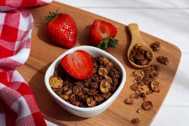 Un bol de granola aux fraises sur une planche en bois