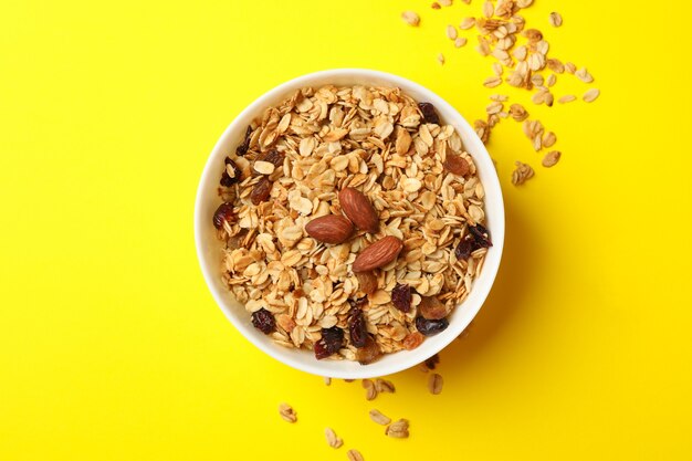 Bol avec granola aux noix et raisins secs sur fond jaune