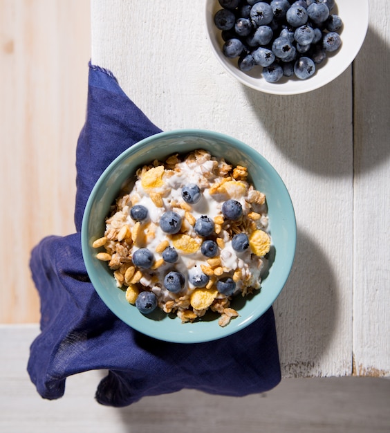 Bol de granola avec du yaourt et des bleuets sur un fond en bois blanc