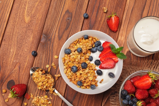 Bol de granola fait maison avec du yaourt et des baies fraîches sur fond en bois