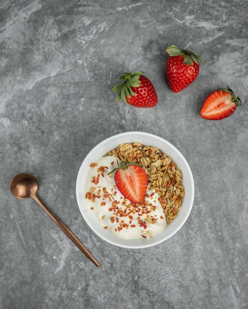 Un bol de granola avec une fraise dessus et une cuillère à côté.