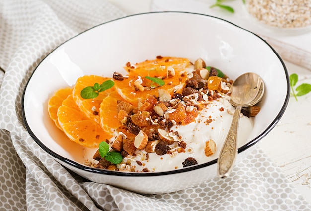 Bol de granola maison avec du yogourt et de la mandarine sur une table en bois blanche. Nourriture de remise en forme.