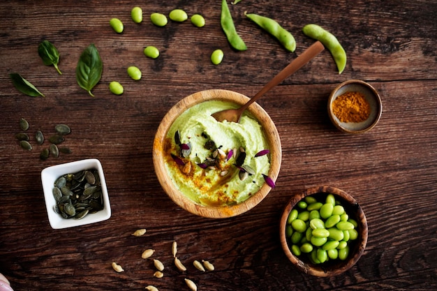 Bol de guacamole avec graines de citrouille et d'edamame gousses de soja et paprika sur une table en bois