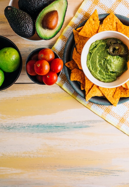 Photo bol de guacamole avec nachos sur table en bois vintage avec des ingrédients frais autour d'elle. copiez l'espace. nourriture végétalienne