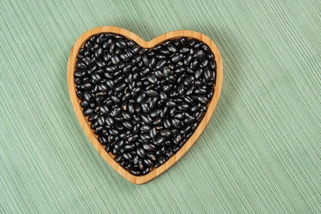 un bol de haricots noirs en forme de cœur sur une nappe verte
