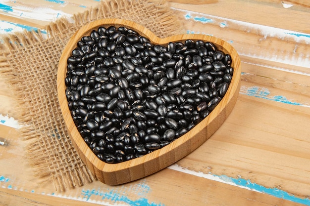 Bol de haricots noirs en forme de coeur sur table en bois